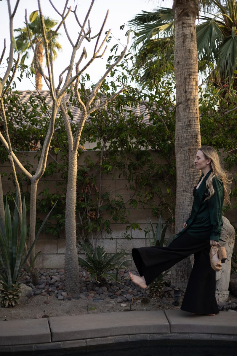Jillian Minter, luxury money mindset coach, walks barefoot beside a tranquil pool in silk loungewear, holding her nude heels with confidence and ease.