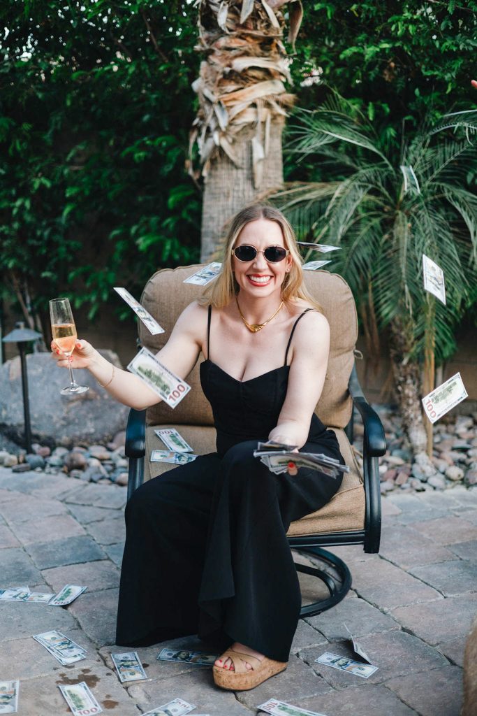 Smiling female coach celebrating prosperity, money flying around her in a high-energy moment holding a champagne glass